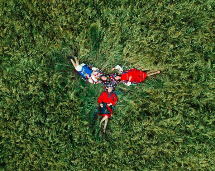 A group relaxing in traditional clothing on a grassy field, captured from above.
